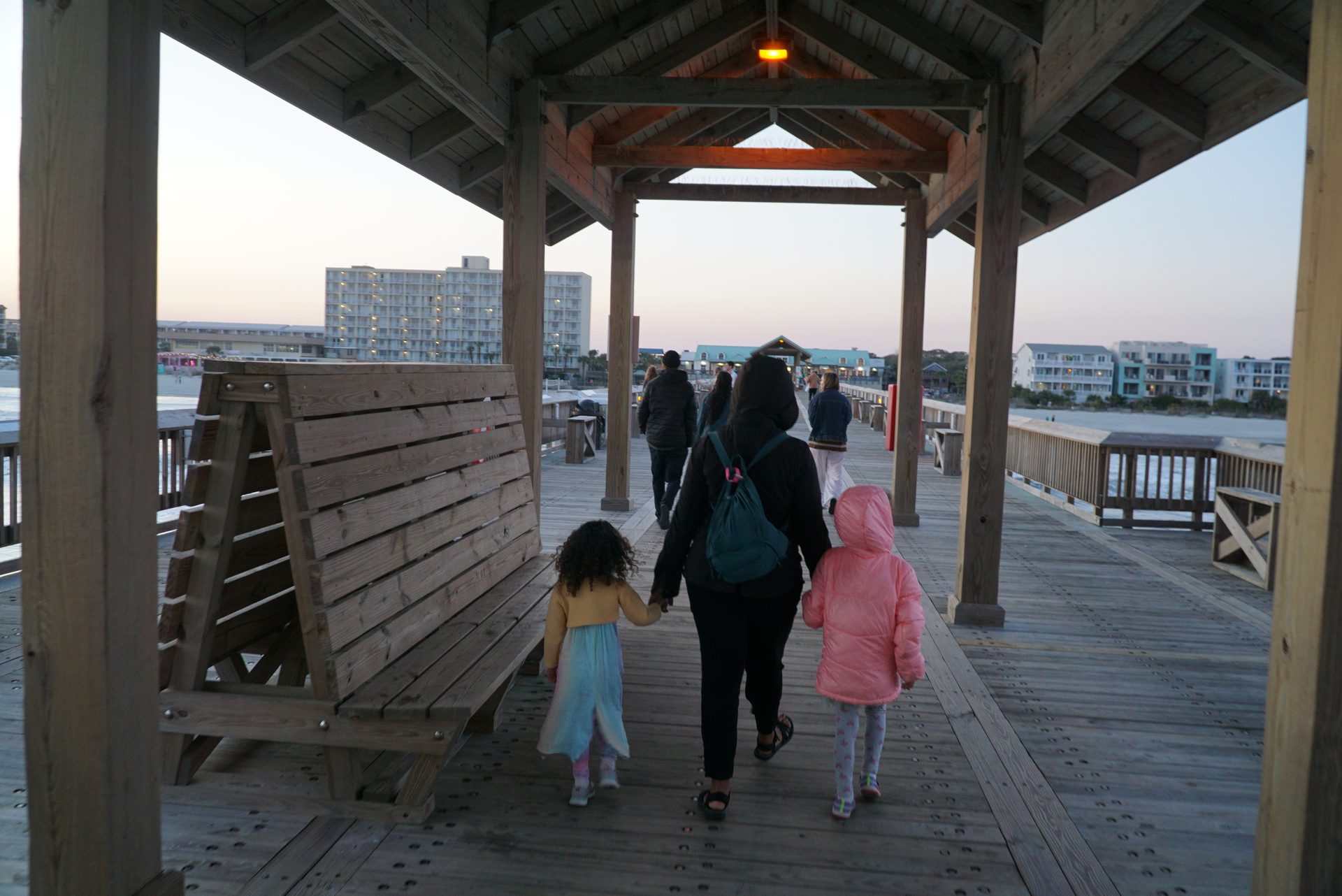Family walking under the Folly Beach pier gazebo at dusk, holding hands