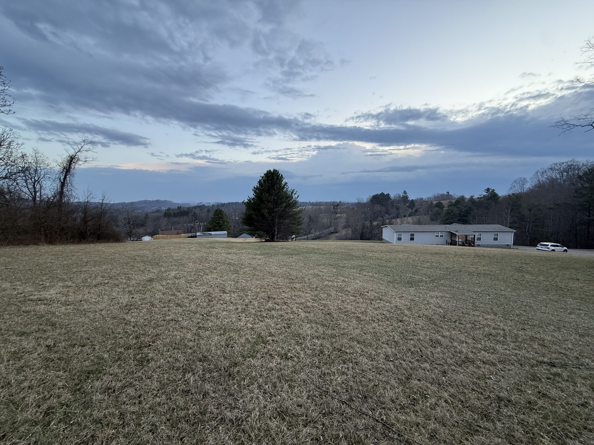 Open field with a ranch house, forested Blue Ridge hills, and dramatic cloud-streaked sky near Galax, Virginia