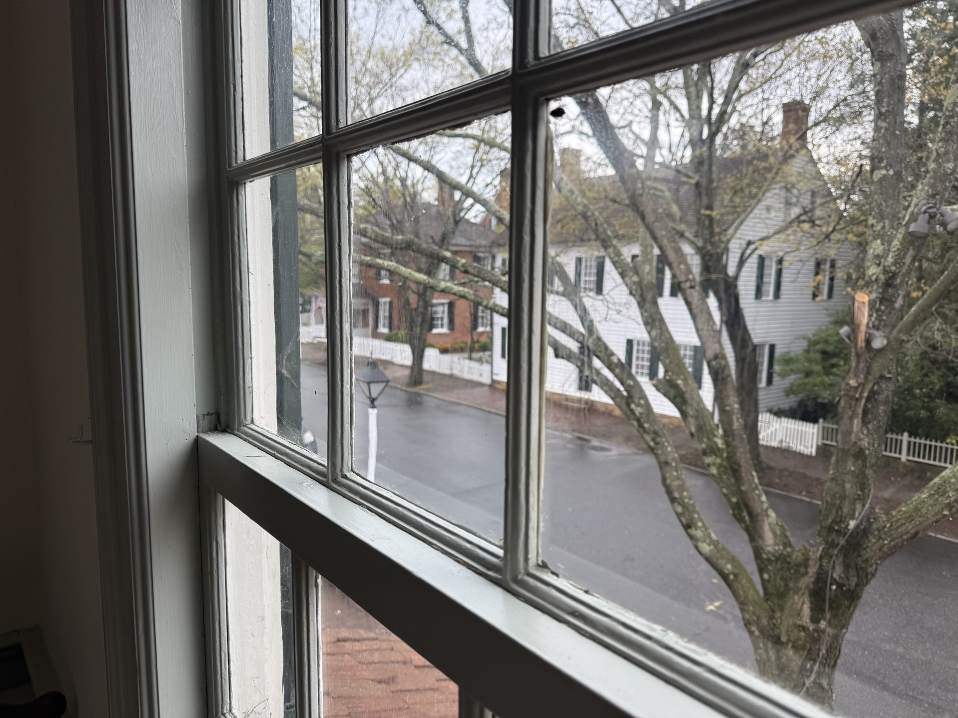 Second-floor window view of rainy Old Salem street lined with colonial-era buildings and bare trees