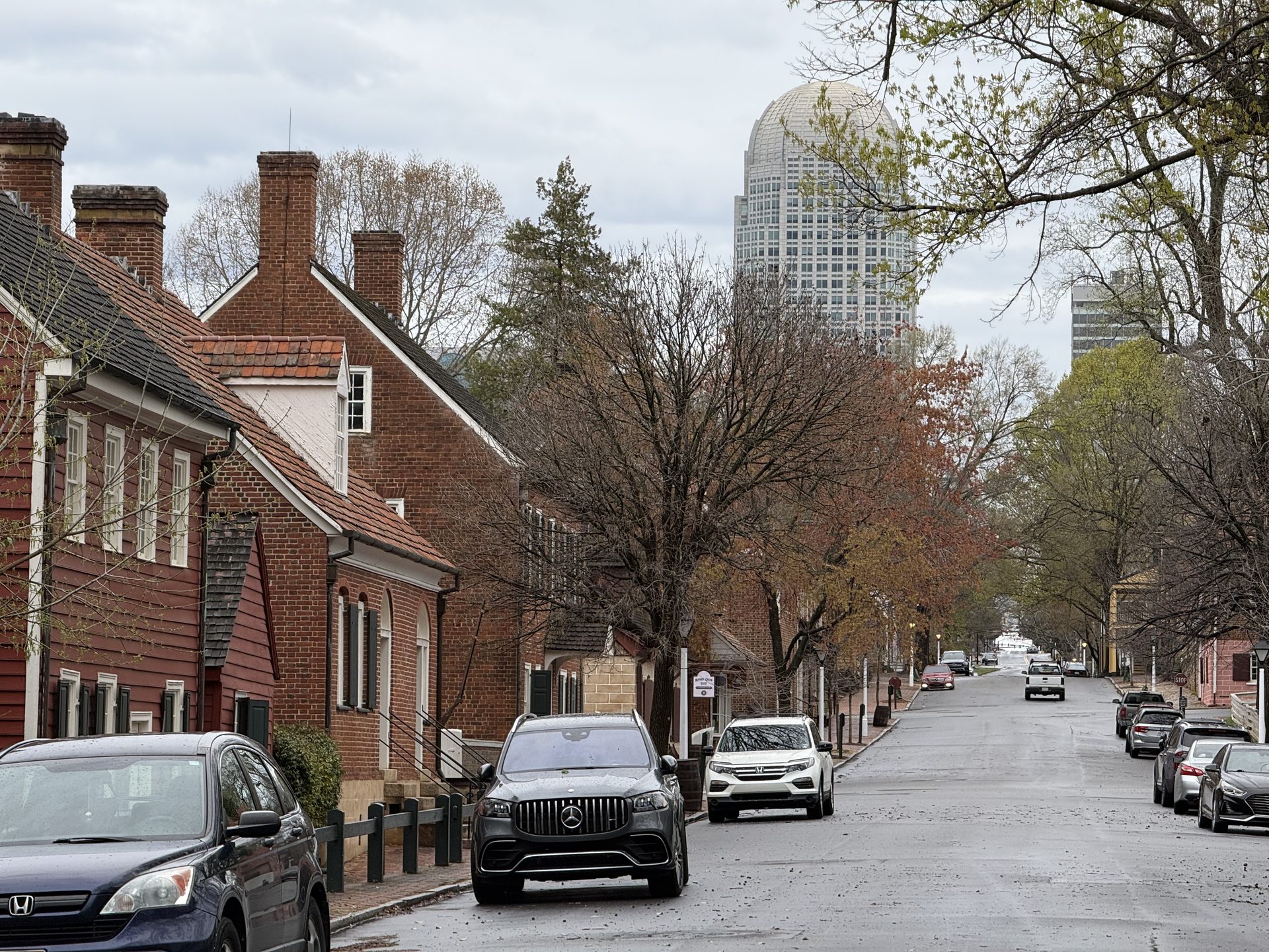 Old Salem's historic corridor with colonial-era brick buildings and a modern Winston-Salem skyscraper glittering in the background