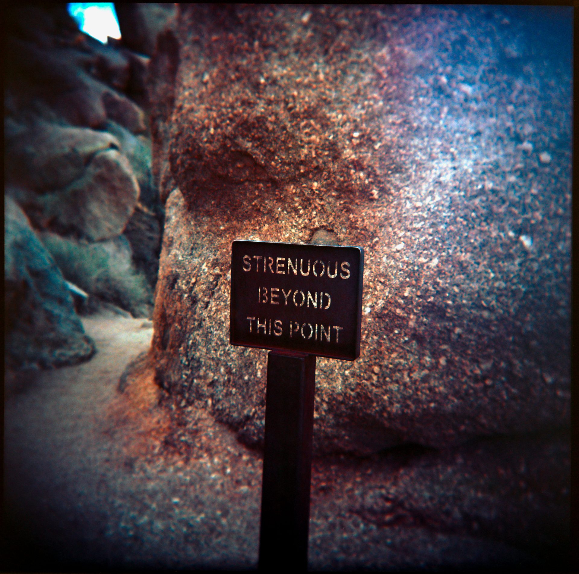 Strenuous Beyond This Point trail sign against a desert boulder — Holga, Ektar 100, Arizona