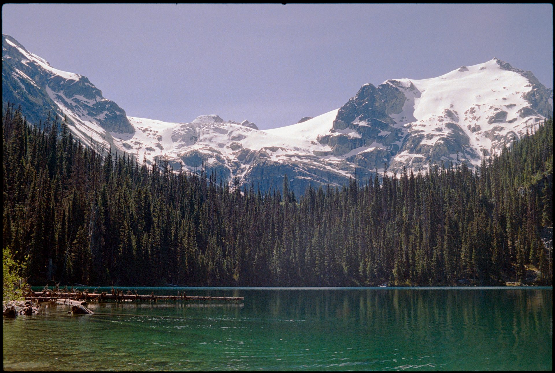 Emerald glacial lake, Joffre Lakes BC — snow-capped peaks and old-growth forest reflecting in still water — Kodak Portra 800