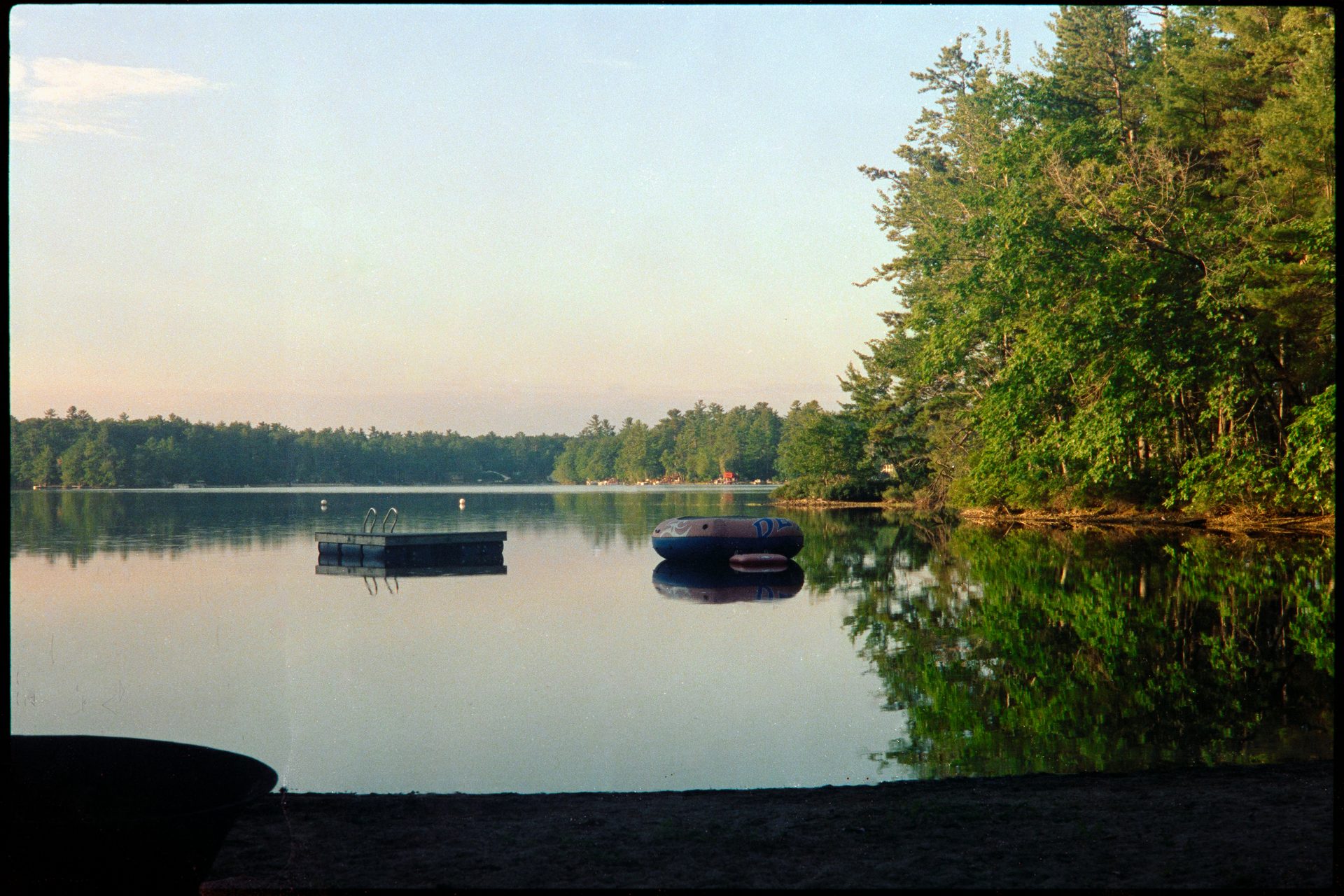 Maine lake at twilight — swimming platform floating on still glassy water — Cinestill 800T