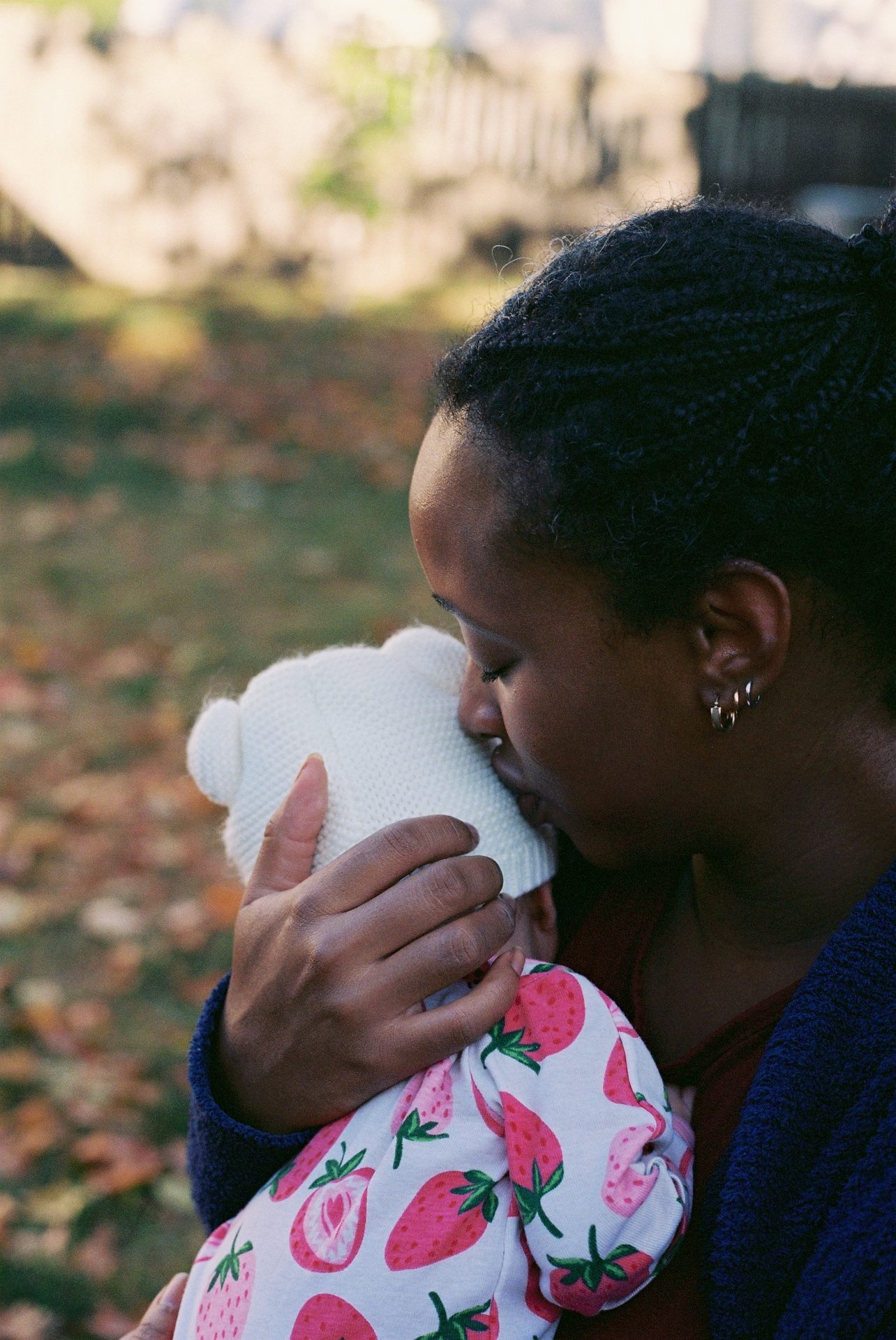 Mother nuzzling her newborn's head in the backyard — shot on 35mm film, natural light