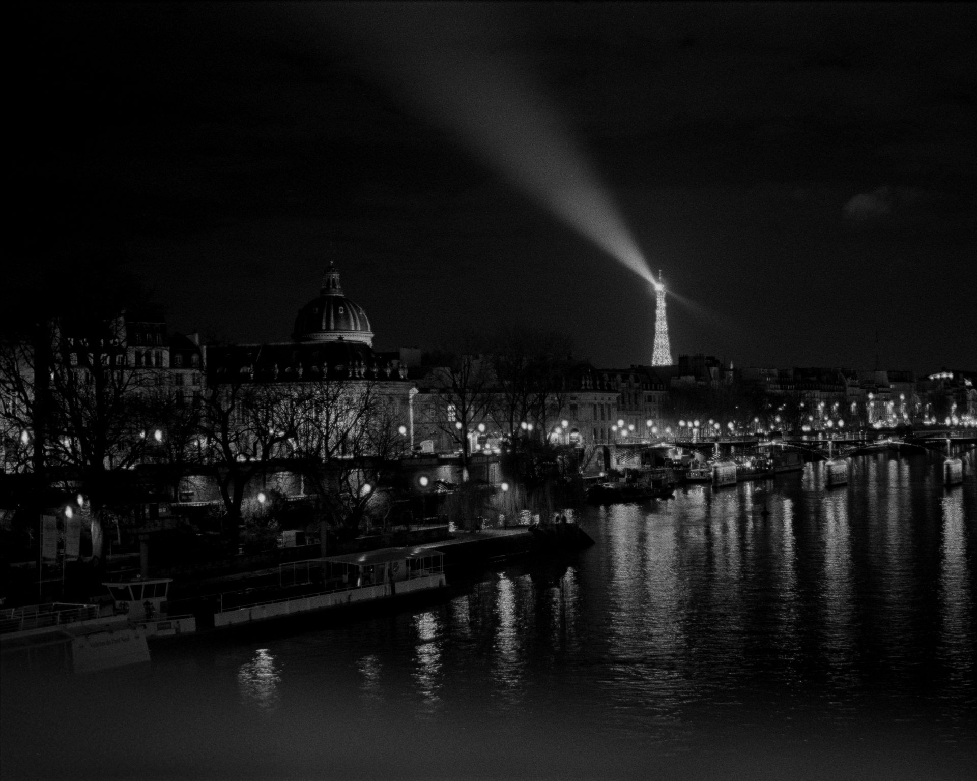 The Eiffel Tower at night, its searchlight sweeping above the Seine — Ilford HP5, 35mm film
