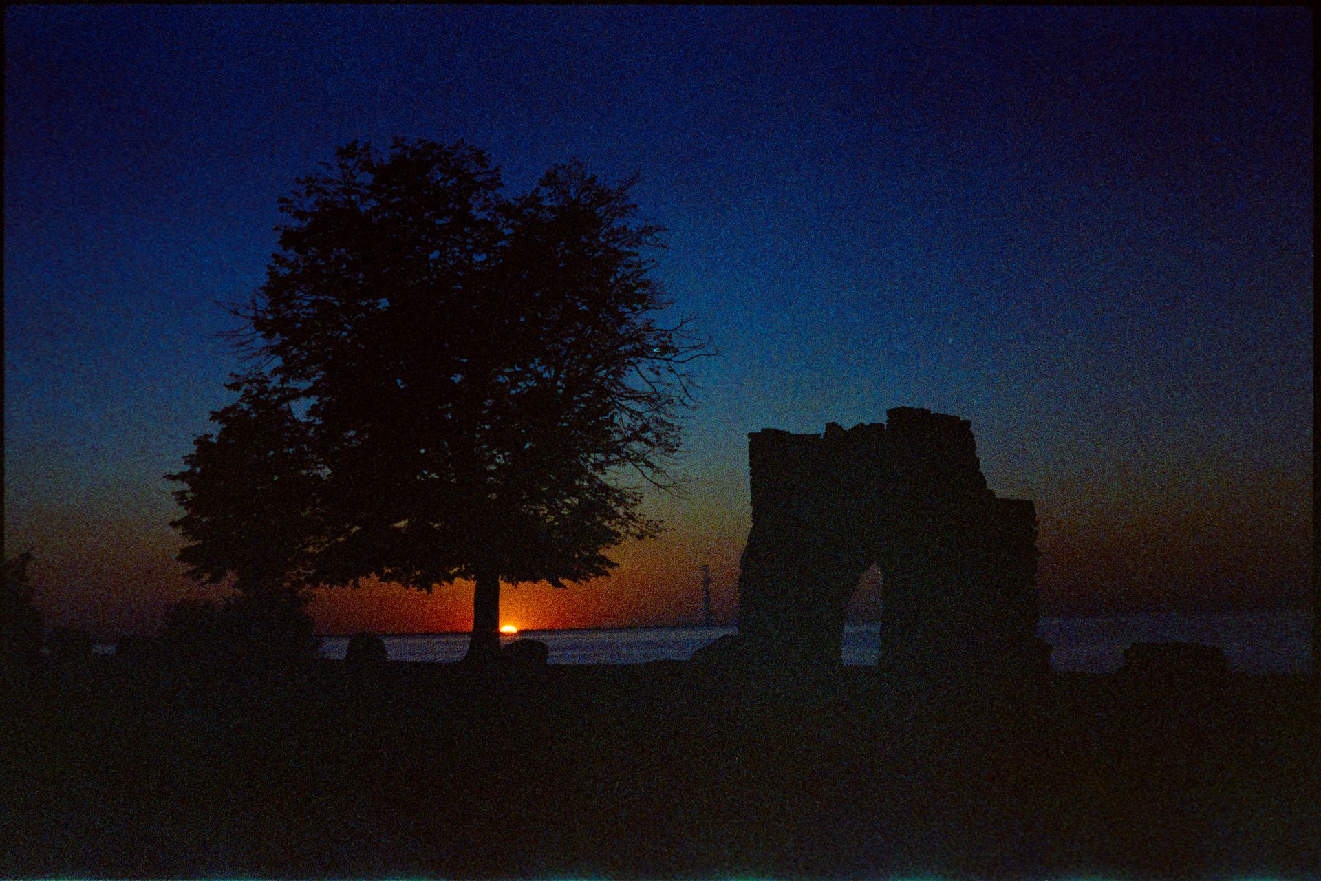 Tree and stone arch silhouetted against a deep sunset at the waterfront — Kodak GC400